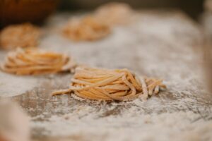 Composition of raw homemade tagliatelle pasta nests placed on wooden table covered with flour in kitchen